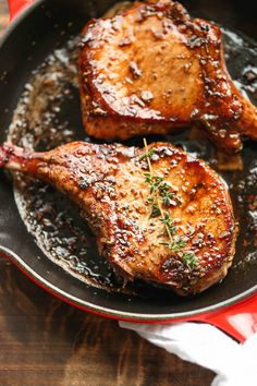 two pork chops in a skillet with sauce and herbs on the side, ready to be cooked