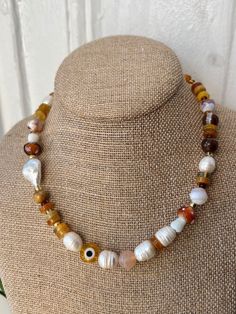 Made in Harlem, inspired by our parks, nature and the life daily grind. This is a one of kind piece, beaded necklace with a large yellow glass evil eye, mix of semi precious stones, glass brown capped mushroom and large beautiful natural freshwater pearls.  This has become an unintentional signature style i love to make. I love to blend the earthy warm colors i see Al day with the semis precious  gemstones contrasting the beautiful genuine freshwater pearls. And the highlight the evil eye for protection. Gold plated clasp closure 16'' inches Unique Everyday Beaded Necklaces, Handmade Spiritual Necklaces For Everyday Wear, Handmade Spiritual Necklace For Everyday Wear, Handmade Spiritual Everyday Necklace, Everyday Spiritual Handmade Necklaces, White Bohemian Beaded Necklace With Evil Eye, Amber Beaded Necklace For Meditation, Yellow Agate Jewelry With Natural Stones, Bohemian White Beaded Necklace With Evil Eye