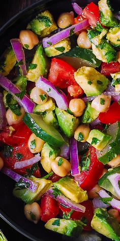 a salad with vegetables and chickpeas is shown in a black bowl on the table