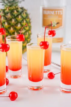 several glasses filled with liquid and topped with cherries next to a pineapple on the table