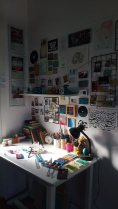 a white desk topped with lots of art and crafting supplies next to a wall covered in pictures