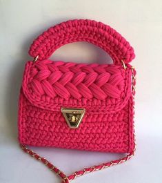 a pink handbag on a white surface with a gold chain hanging from the handle