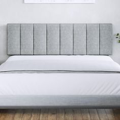 a bed with a gray headboard and white sheets in front of a painting on the wall