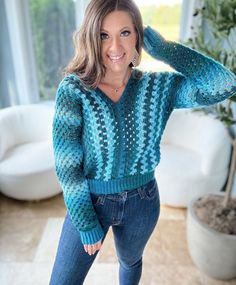 a woman is posing for the camera in her living room wearing a blue sweater and jeans