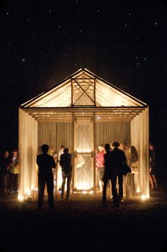 people standing in front of a small structure with lights on it at night, surrounded by other people