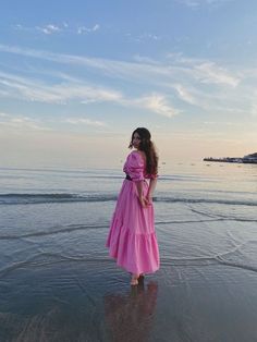 a woman in a pink dress is standing on the beach and looking into the distance