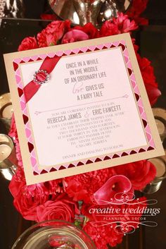 a pink and white wedding card with red flowers in the center is surrounded by candles