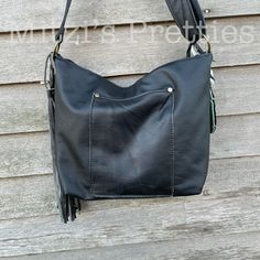 a black leather purse hanging on the side of a building with a tasselled handle