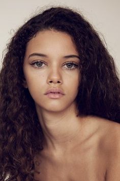 a woman with long curly hair is looking at the camera while wearing a bra top