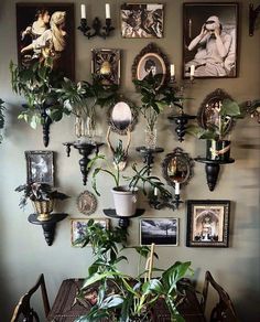 a dining room table with plants and pictures on the wall above it, along with candles