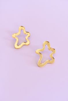 two gold earrings on a purple surface with one in the shape of a star and another in the shape of a flower