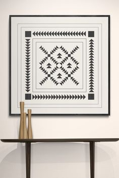 two vases are sitting on a table in front of a wall hanging with black and white designs