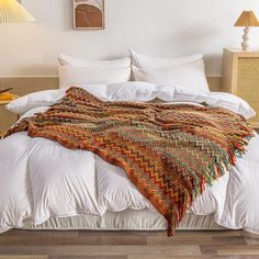 a bed with white sheets and blankets on top of it in a bedroom next to two lamps