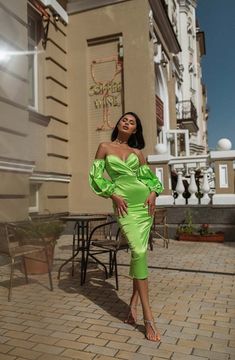 a woman standing in front of a building wearing a green dress with puffy sleeves