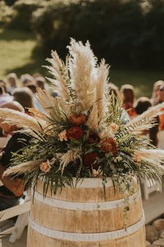 a wooden barrel with flowers and greenery on it in front of an outdoor ceremony