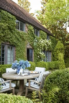 an outdoor table and chairs in front of a house with ivy covered walls on either side