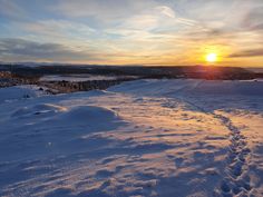 the sun is setting over some snow covered hills with tracks in the snow and trees