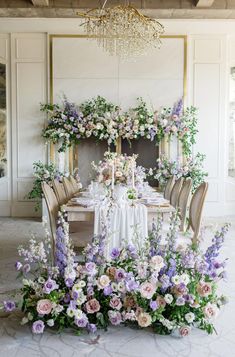 a dining table with flowers and greenery on the top is surrounded by gold chairs