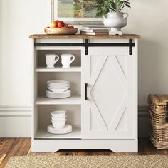 a white cabinet with plates and cups on it next to a basket full of fruit