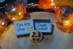 a cookie is sitting on top of a wooden table with some lights around it and a sign that says you are one tough cookie