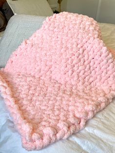 a pink crocheted blanket laying on top of a bed next to a pillow