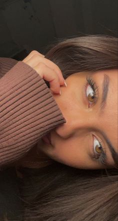 a close up of a woman with brown hair and blue eyes holding her hand to her face