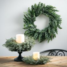 two candles are sitting on a table next to a wreath