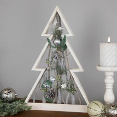 a christmas tree made out of branches and pine cones on a table next to candles