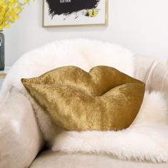 a gold pillow sitting on top of a white couch next to a vase with yellow flowers