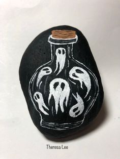 a black rock with white paint on it that has a painted image of two witches in a bottle