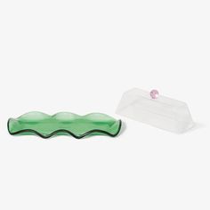 a green object sitting next to a plastic container on a white surface with a pink bead in it