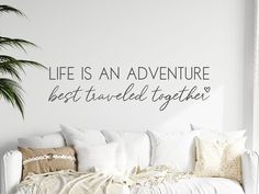 a living room with a white couch and wall decal that says life is an adventure best traveled together