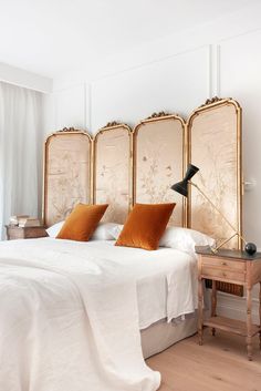 a white bed topped with orange pillows next to two mirrors and a table in front of it