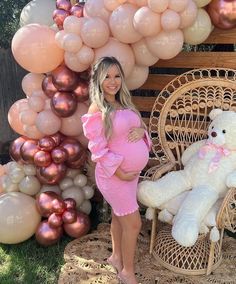 a pregnant woman standing next to a giant teddy bear in front of balloons and chairs