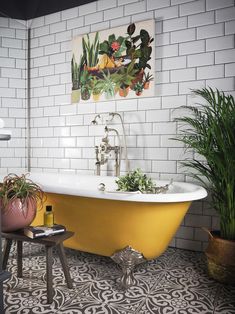 a yellow bath tub sitting next to a green plant in a white tiled bathroom with potted plants on the floor