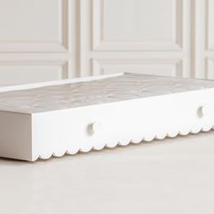 a white bed frame with scalloped edges and buttons on the bottom, in front of a wall