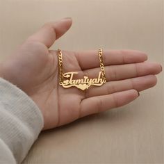 a person's hand holding a gold necklace with the word, tamukh on it