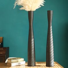 two tall vases sitting on top of a wooden table next to a blue wall