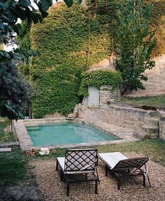 two lawn chairs sitting next to a pool in the middle of a yard with ivy covered walls