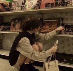 a woman sitting on the ground in front of a book shelf holding onto a purse