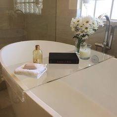 a white bath tub sitting next to a window with flowers in it and a book on the edge