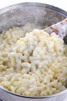 macaroni and cheese is being stirred with a wooden spoon in a metal bowl