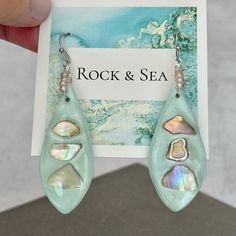 These beachy aqua earrings are handmade with great attention to detail, and each pair is one of a kind. Polymer clay is expertly mixed to a beautiful shade of aqua, cut into teardrop shapes, embedded with iridescent shell chips, and brushed with a shimmer powder to really catch the light. The earrings were baked, sanded, drilled, then resin applied to the fronts to create a glossy, elegant finish. Wire wrapped circles of pale pink seed beads have been added to the tops of the earrings for an extra decorative touch. The earrings hang approximately 2.5 inches from the top of the Stainless Steel ear wires. Choose your exact pair at checkout, using the 6th and 7th photo as reference. These unique earrings would make a wonderful gift for someone who loves the beach. At checkout, you may choose Unique Nickel-free Earrings For Beach, Unique Beaded Drop Earrings For Beach, Unique Drop Earrings For Beach, Blue Dangle Earrings For The Beach, Beach Teardrop Beaded Earrings, Unique Blue Earrings For Beach, Blue Shell-shaped Earrings For Beach, Beach Teardrop Beaded Earrings For Pierced Ears, Handmade Light Blue Beach Earrings