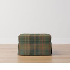 a green and orange plaid ottoman sitting on top of a hard wood floor next to a white wall