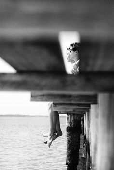 black and white photograph of woman jumping off dock into water from pier with ocean in background