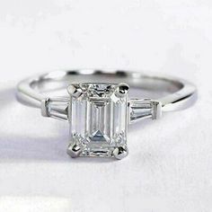 an emerald - cut diamond ring with baguets on the shoulders and side stones