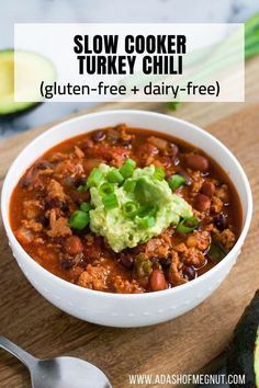 a bowl of slow cooker turkey chili with avocado on top and the text overlay reads, slow cooker turkey chili gluten - free + dairy - free