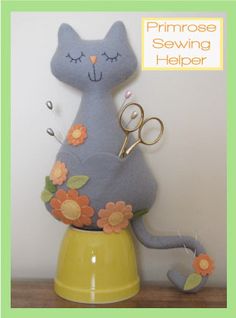 a blue cat sitting on top of a yellow vase with scissors in it's mouth