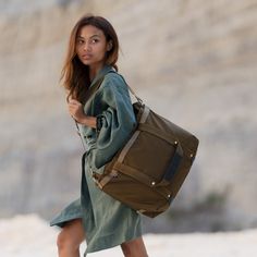 a woman carrying a brown duffel bag while walking down the street with her foot in the air