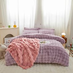 a bed with pink and purple comforters in a bedroom next to a window,